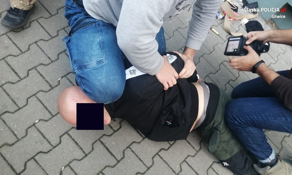 Dwóch policjantów po cywilnemu obezwładniło na chodniku podejrzanego - łysego mężczyznę. policjant po prawej przeszukuje jego rzeczy