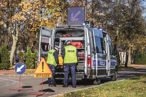 na zdjęciu dwóch policjantów w kamizelkach odblaskowych stoi przodem do samochodu marki volkswagen crafter 2,0 TDI tachimetr, przed nimi stoją dwa znaki drogowe