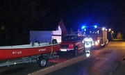 wozy strażackie i łódź motorowa stojące przy drodze, drogą idący strażak