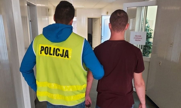 policjant w żółtej odblaskowej kamizelce  prowadzi zatrzymanego mężczyznę