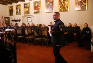 wnętrze pomieszczenia, policjanci siedzą przy stole słuchając wykładu