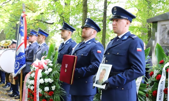 policjanci przed kościołem trzymają w rękach zdjęcie zmarłego i odznaczenie