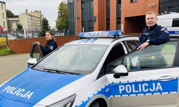 policjant i policjantka stoją przy radiowozie