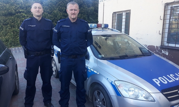 dwóch policjantów stoi przy oznakowanym radiowozie