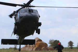 Policyjny śmigłowiec Black Hawk podchodzi do lądowania, mężczyzna w czerwonym kasku daje znaki pilotowi.