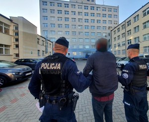 Policjanci doprowadzający przez plac zatrzymanego