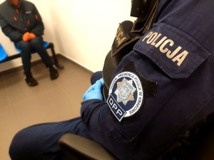 Policjant z naszywką na mundurze z napisem Oddział Prewencji w Krakowie, w tle zatrzymany mężczyzna