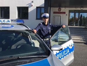 Policjant stoi przy radiowozie. W tle budynek jednostki