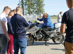 mężczyzna siedzi na motocyklu, przed nim stoi grupka mężczyzn