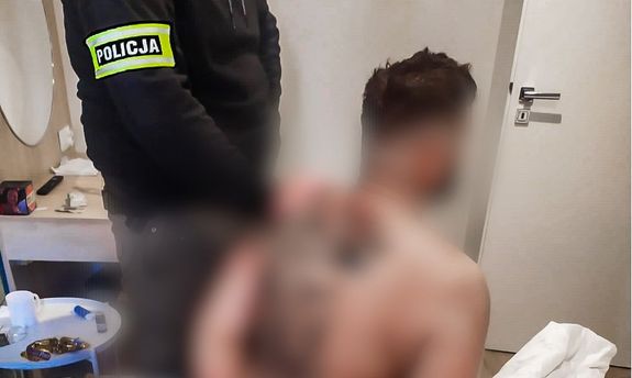 Policjant operacyjny z zatrzymanym mężczyzną, który ma nagi tors i siedzi na łóżku