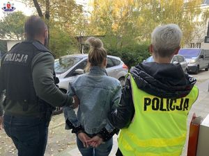 policjant w czarnej kamizelce z napisem Policja i policjantka w żółtej kamizelce z napisem Policja prowadzą zatrzymaną kobietę