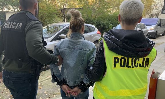 policjant w czarnej kamizelce z napisem Policja i policjantka w żółtej kamizelce z napisem Policja prowadzą zatrzymaną kobietę