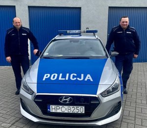 dwaj umundurowani policjanci stoją przy radiowozie