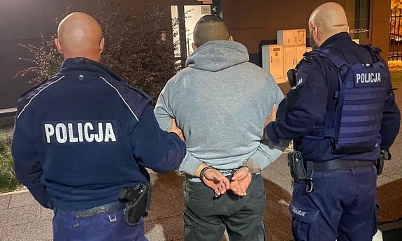 dwóch umundurowanych policjantów prowadzi zatrzymanego mężczyznę