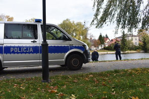 Policjanci wyławiają z kanału mężczyznę. Z boku widać zaparkowany policyjny furgon