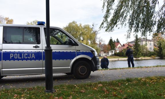 Policjanci wyławiają z kanału mężczyznę. Z boku widać zaparkowany policyjny furgon