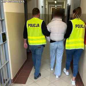 dwaj policjanci w żółtych kamizelkach prowadzą zatrzymaną kobietę