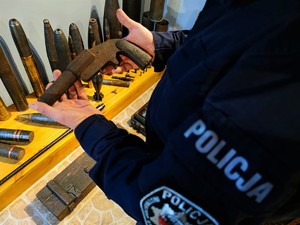 Zdjęcie kolorowe przedstawia zabytkowy pistolet w rękach policjanta