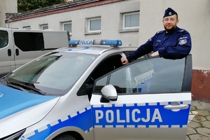 umundurowany policjant stoi w  otwartych drzwiach radiowozu