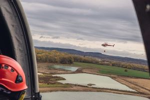 widok przez okno z pokładu policyjnego  śmigłowca na inny śmigłowiec w locie który transportuje bambi bucket