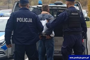 umundurowani policjanci prowadzą do radiowozu zatrzymanego mężczyznę