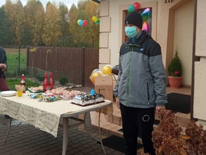 chłopiec stoi przed domem, obok chłopca stoi stół z tortem urodzinowym i przekąskami