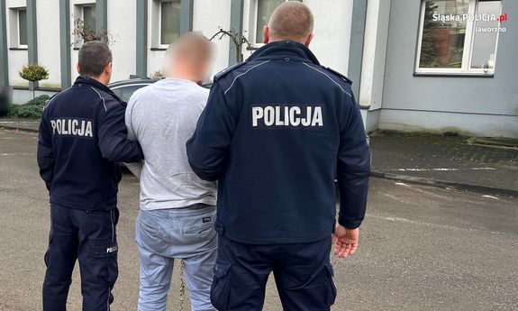 Dwaj umundurowani policjanci stoją przed komendą z zatrzymanym