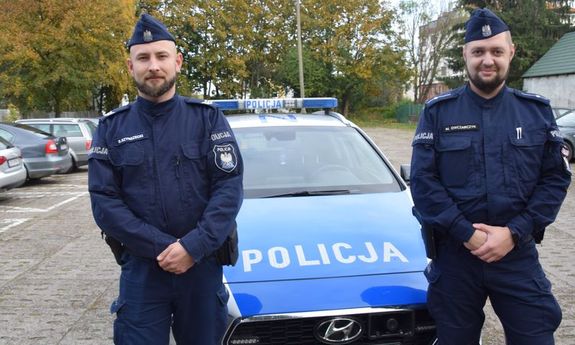 dwaj umundurowani policjanci przy radiowozie