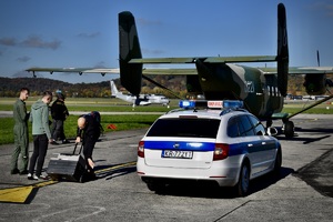 mężczyźni stoją na płycie lotniska obok pojazdu służbowego z napisem transplantacja, jeden z mężczyzn prowadzi walizkę do samolotu