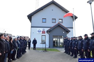 zebrani funkcjonariusze i osoby cywilne stoją w dwóch rzędach na przeciwko siebie przed nową siedzibą posterunku Policji