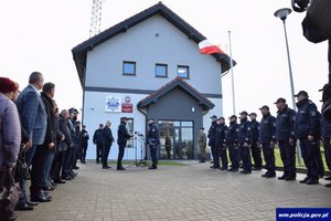 zebrani funkcjonariusze i osoby cywilne stoją w dwóch rzędach na przeciwko siebie przed nową siedzibą posterunku Policji