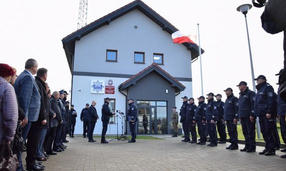 zebrani funkcjonariusze i osoby cywilne stoją w dwóch rzędach na przeciwko siebie przed nową siedzibą posterunku Policji