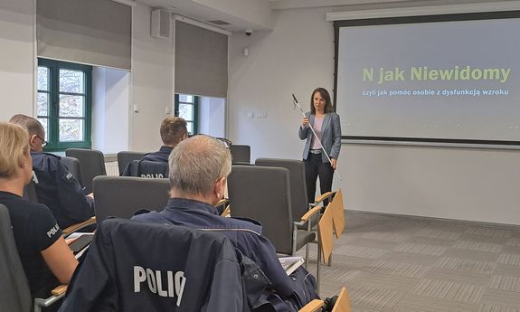 policjanci podczas szkolenia. Prowadząca stoi na przeciwko nich i trzyma w ręku białą laskę