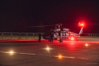 Policyjny śmigłowiec Black Hawk na lądowisku nocą, ma zapalone świata ostrzegawcze.