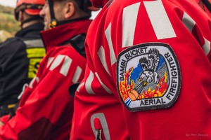 Plakietka Bambi Bucket Aerial Firefighter przedstawiająca orła niosącego w szponach podwieszany na linach pojemnik na wodę.