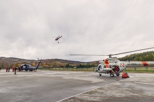 Policyjny śmigłowiec Black Hawk i śmigłowiec Sokół Straży Granicznej na lądowisku, w oddali unoszący się czerwony śmigłowiec Straży Pożarnej.