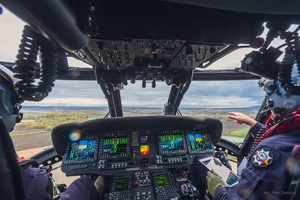 Piloci w kabinie lecącego policyjnego śmigłowca Black Hawk, na środku konsola z ekranami komputerowymi wskazującymi parametry lotu.