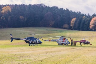 Trzy śmigłowce na trawiastym lądowisku, pomiędzy nimi grupka mężczyzn.