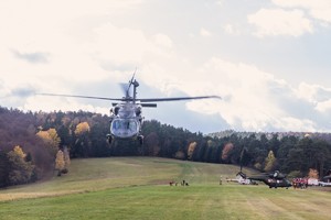 Policyjny śmigłowiec Black Hawk nad trawiastym lądowiskiem, w dole dwa inne śmigłowce i samochód straży pożarnej.