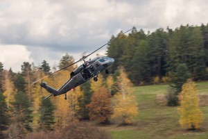 Policyjny śmigłowiec w dynamicznym locie Black Hawk na tle terenów leśnych.