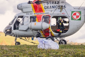 Śmigłowiec Sokół Straży Granicznej na trawiastym lądowisku, z tylnego luku wygląda mężczyzna.