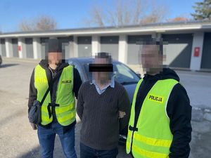 dwaj policjanci prowadzą zatrzymanego mężczyznę zakutego w kajdanki