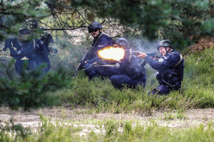 policjanci ukrywający się w zaroślach, jeden z nich oddaje strzał z broni służbowej