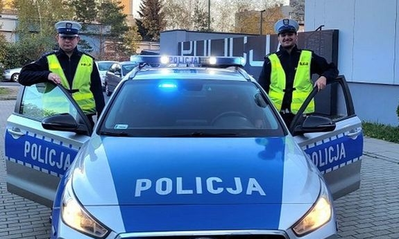 dwaj policjanci stoją przy radiowozie