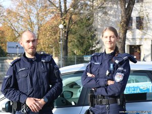 policjant i policjantka stoją przy radiowozie