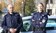 policjant i policjantka stoją przy radiowozie