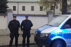 dwaj umundurowani policjanci stoją przy policyjnym furgonie