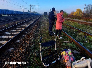 Policjant pomaga kobiecie zejść z torowiska