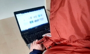 zdjęcie poglądowe: mężczyzna w czerwonej kamizelce z kapturem na głowie siedzi przed komputerem