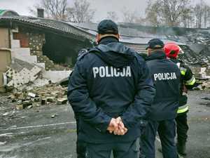 policjanci i strażacy na miejscu zdarzenia, w tle uszkodzony budynek